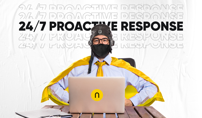 The image shows a person sitting at a wooden table with a laptop open in front of them. The person is wearing glasses, a b...