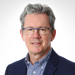 Professional headshot of a mature man wearing glasses and a blazer