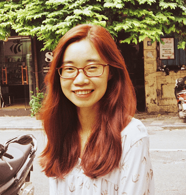 Young woman with red hair and glasses smiling outdoors near a motorcycle