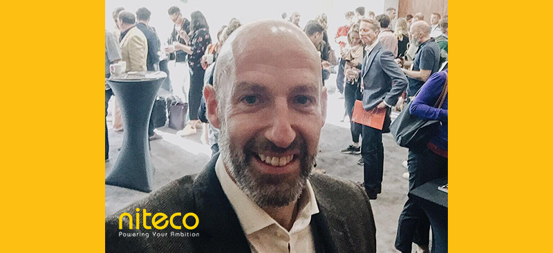 Smiling man at Niteco networking event with attendees in the background