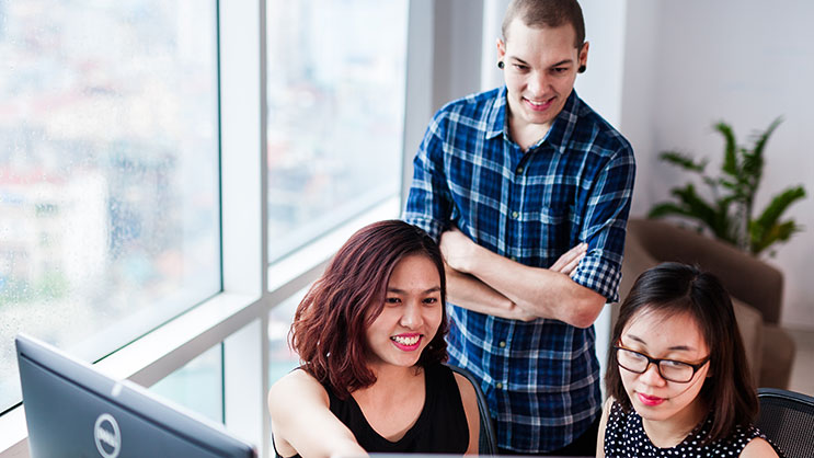 Three colleagues collaborating at a computer in a bright office setting