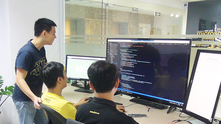 Developers collaborating on programming code displayed on multiple monitors in office