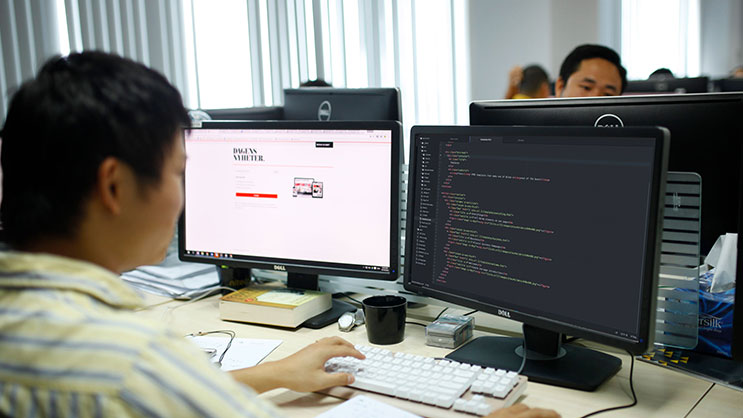 Developer coding website on dual monitors in modern office workspace