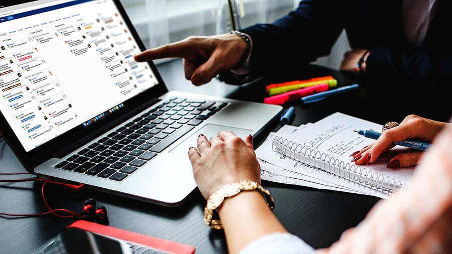 Hands pointing at laptop with project management software and notes on desk