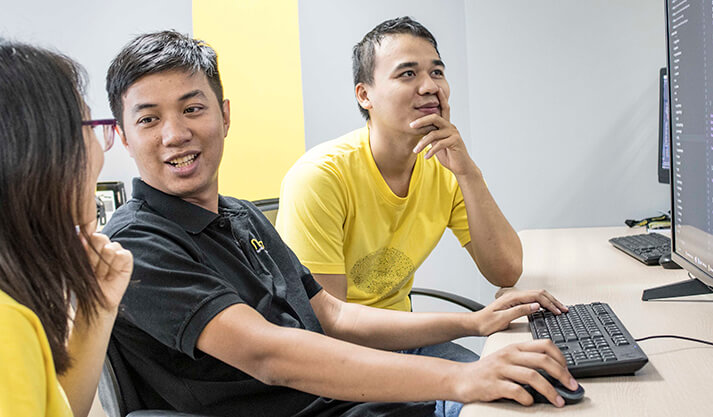 Three colleagues collaborating on software development at a computer desk