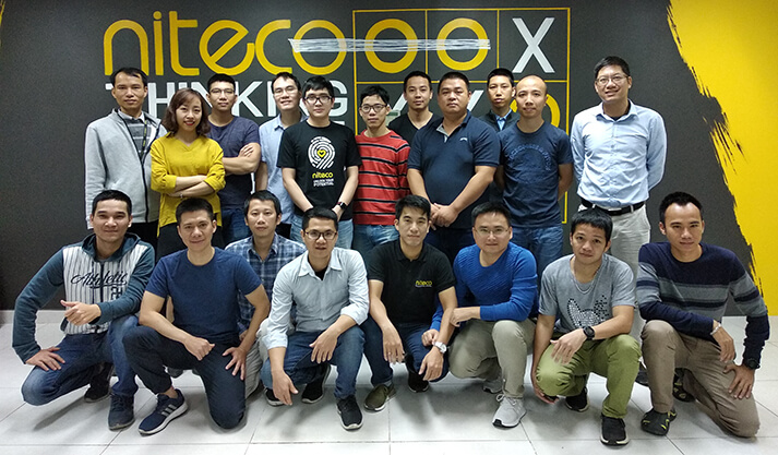 Team members posing in front of Niteco HackerX logo wall for group photo