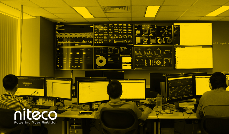 Three IT professionals monitoring multiple screens displaying data analytics dashboards