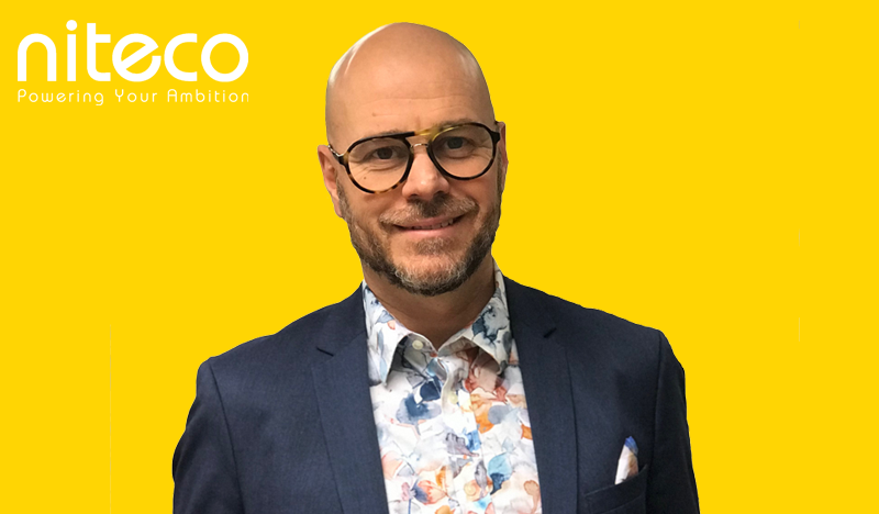 Man in glasses and floral shirt representing Niteco on a yellow background