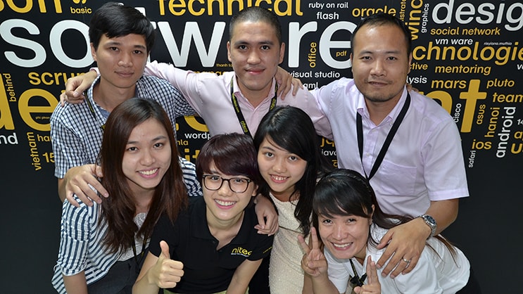 seven smiling software team members posing with thumbs up and peace signs